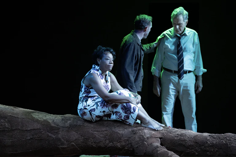 Two men and a woman on stage, lit by an eerie bluish-green light.