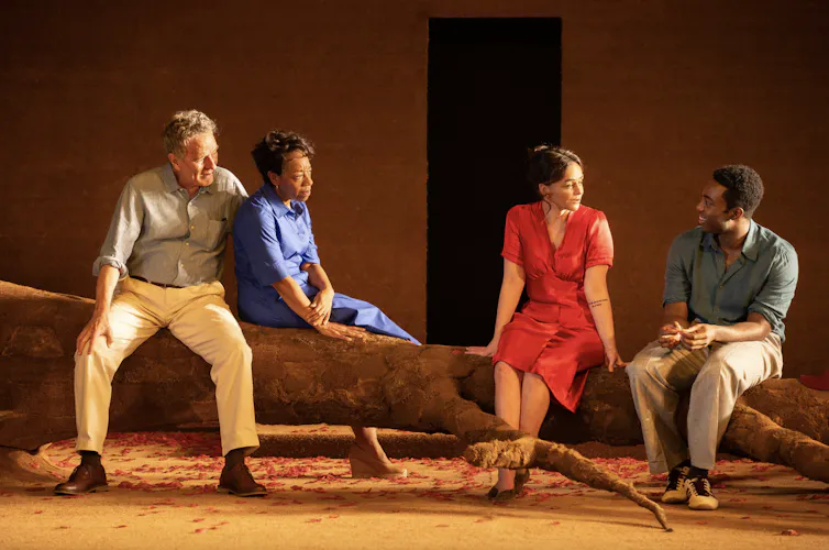 Four people on stage sitting on a large tree trunk.