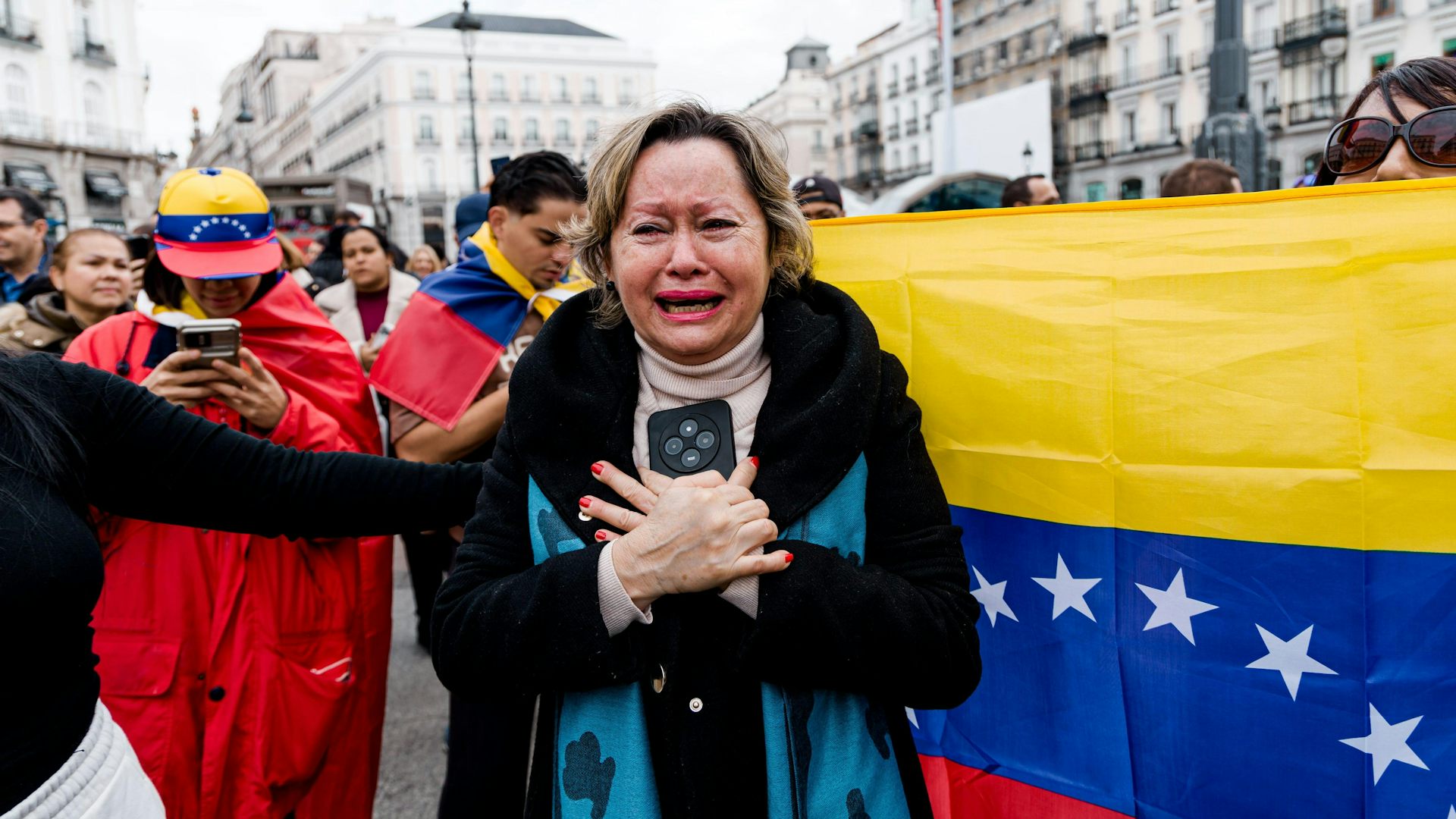 Una mujer llora con una bandera de Venezuela detrás.