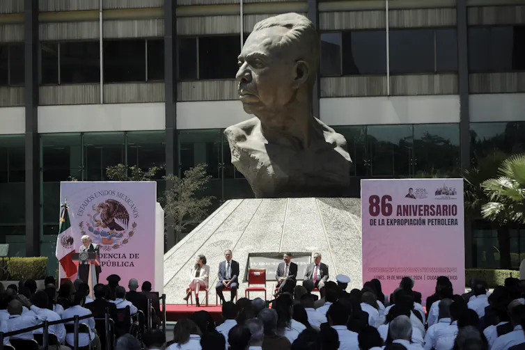 A crowd in Mexico gathers for a speech below a large bust of a man.