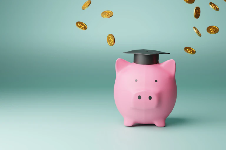 A pink piggy bank is seen with a black graduation cap and coins around it.
