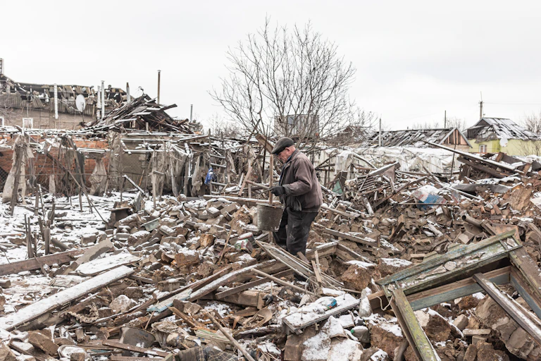 A man holding a bucket walks through rubble.