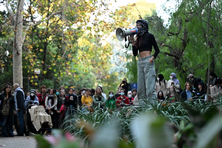 A young woman with a megaphone stands on a platform and speak to a protest rally