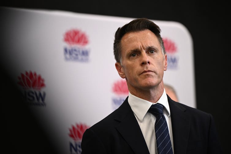 A man in a suit stands in front of a NSW government backdrop