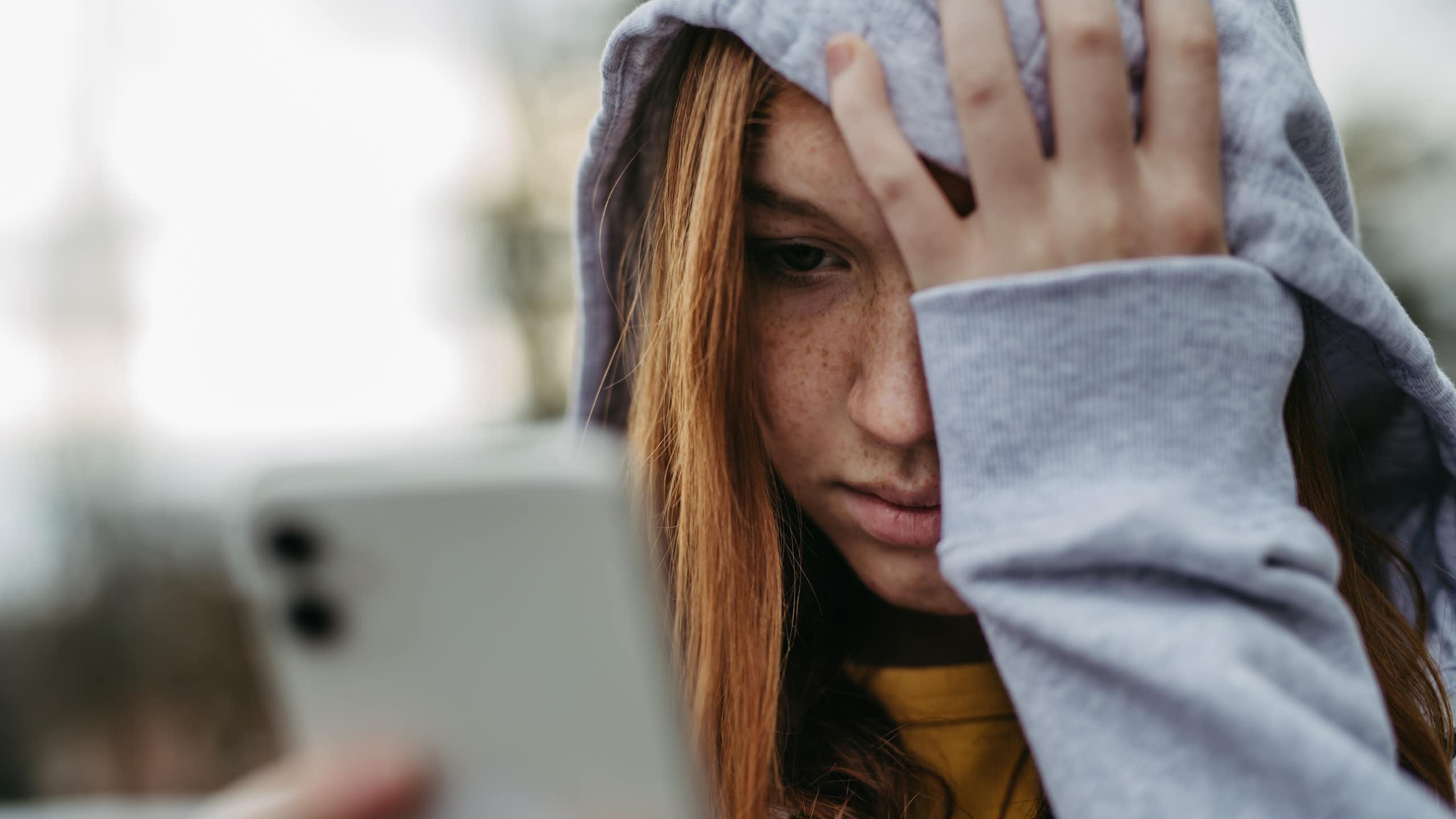 Une adolescente en train de regarder son téléphone portable se tient la tête.