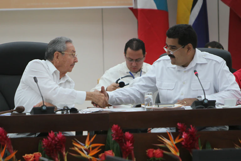 Two men in white shirts shake hands while sitting at a table.