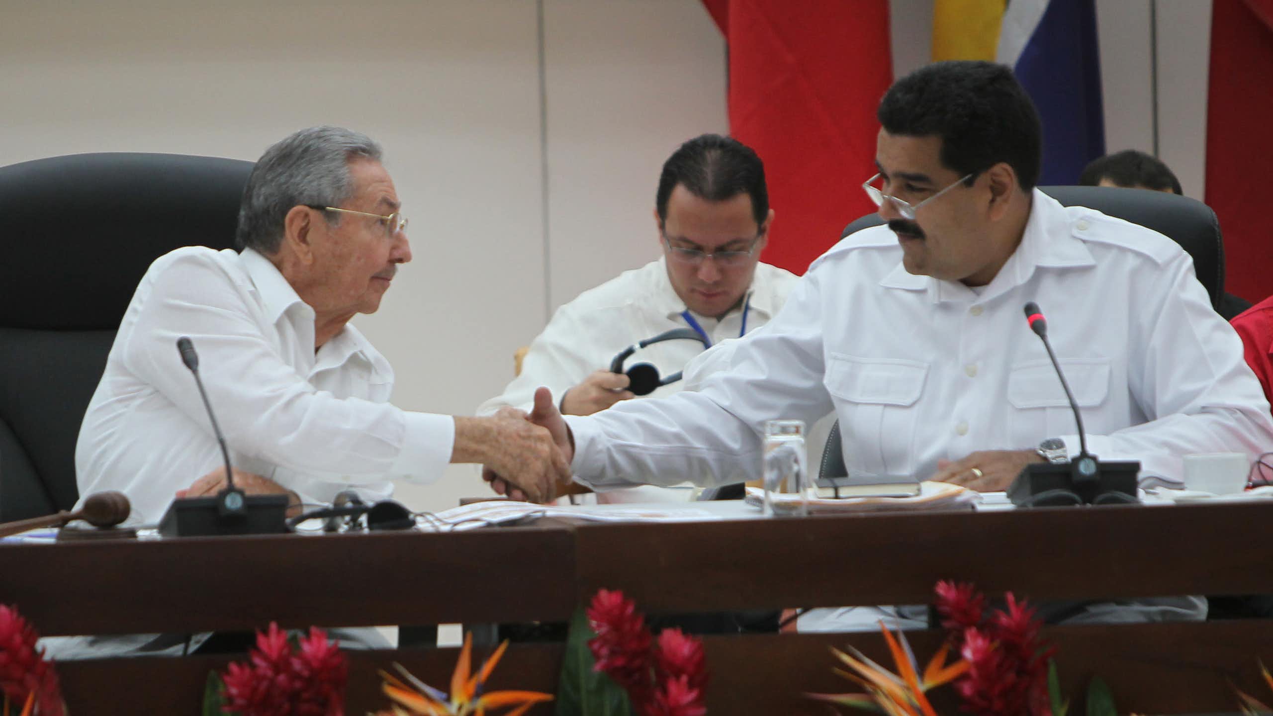 Two men in white shirts shake hands while sitting at a table.