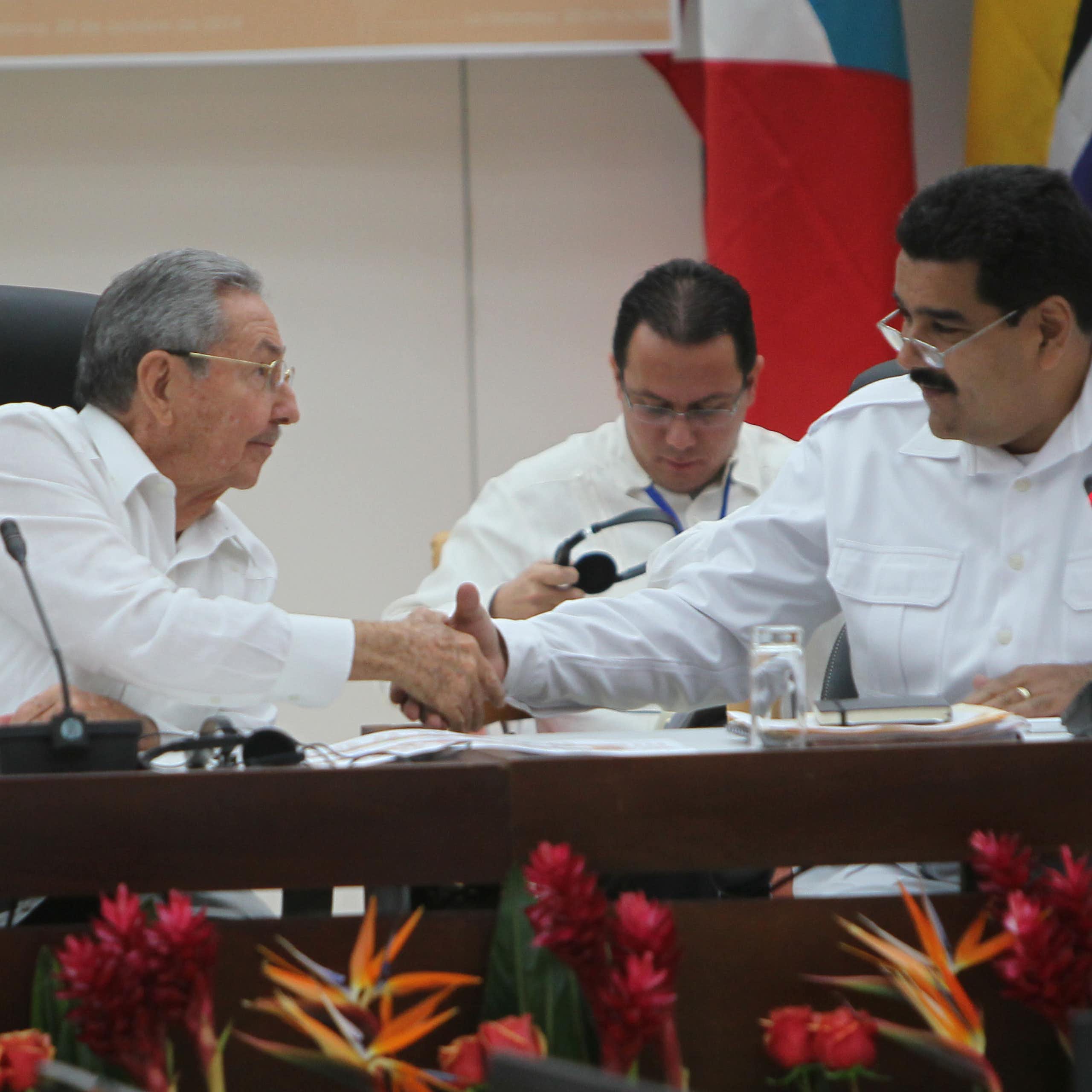 Two men in white shirts shake hands while sitting at a table.