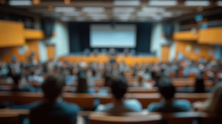 A blurred image of students in a lecture theatre taken from behind them.