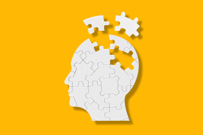 The side profile of a head made out of puzzle pieces. Some pieces are missing from the centre of the head, which have been scattered above it.