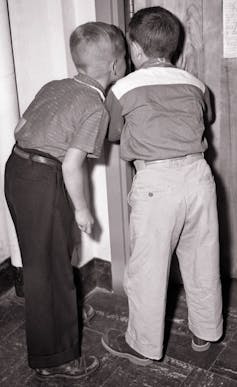 Vintage photograph of two young boys peering through a crack in a door.