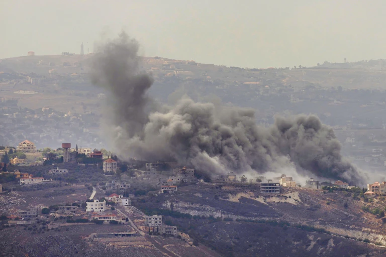 Smoke rises over a hilly rural landscape.