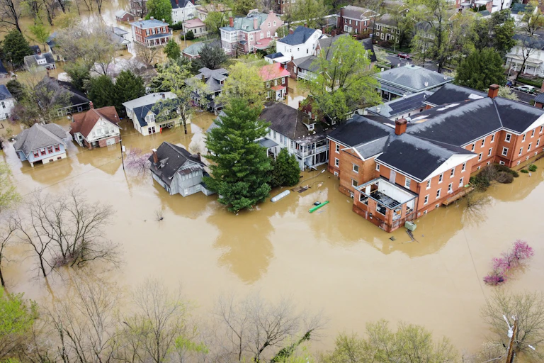 A view of muddy river water surrounding more than a dozen homes and a large brick building in Frankfort. A kayaker can be seen near one of the buildings.