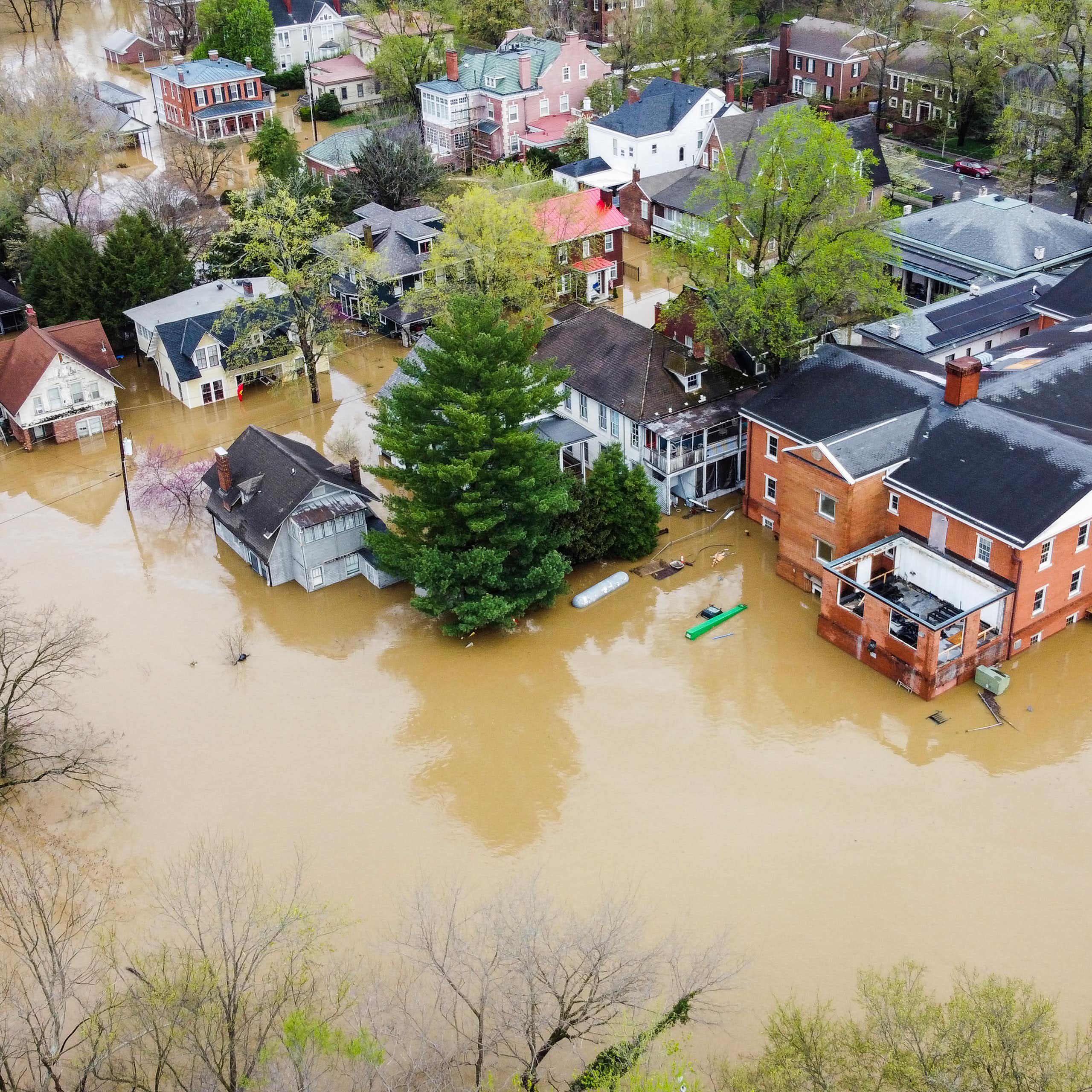 A view of muddy river water surrounding more than a dozen homes and a large brick building in Frankfort. A kayaker can be seen near one of the buildings.