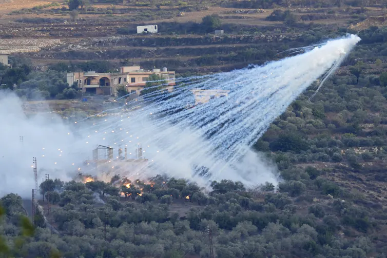 White smoke billows over a field on fire.
