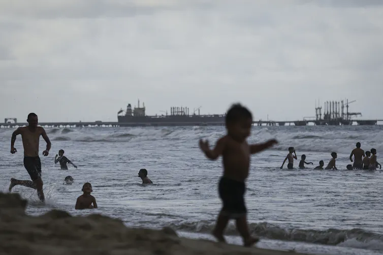 People spend time on a beach with an oil tanker nearby.