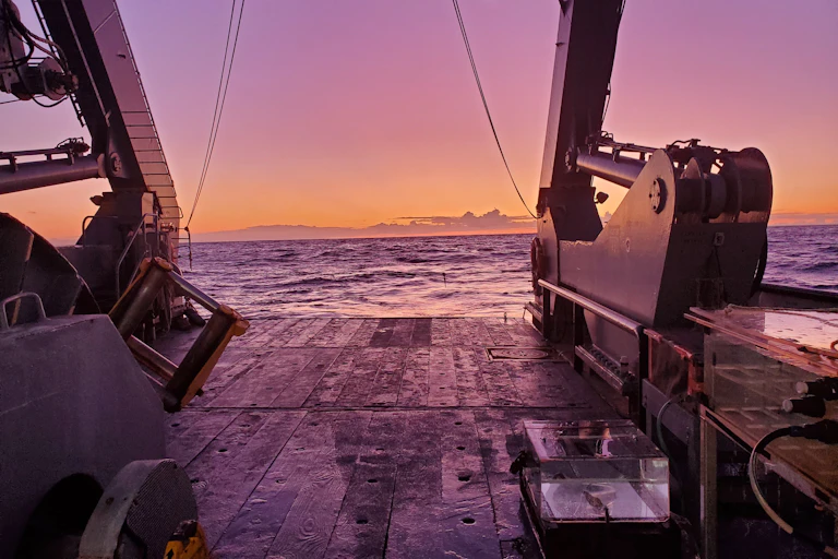 Looking off the back of a ship to the ocean at sunset.