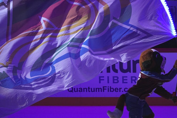 Una persona con la mascota de San Bernardo patina sosteniendo una bandera con el logo de Colorado Avalanche
