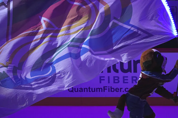 A person in a St. Bernard mascot suit skates while holding a flag with the Colorado Avalanche logo on it