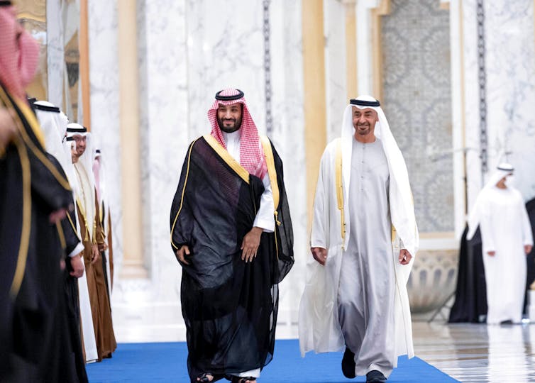 Two men in Gulf Arab attire walk side by side.