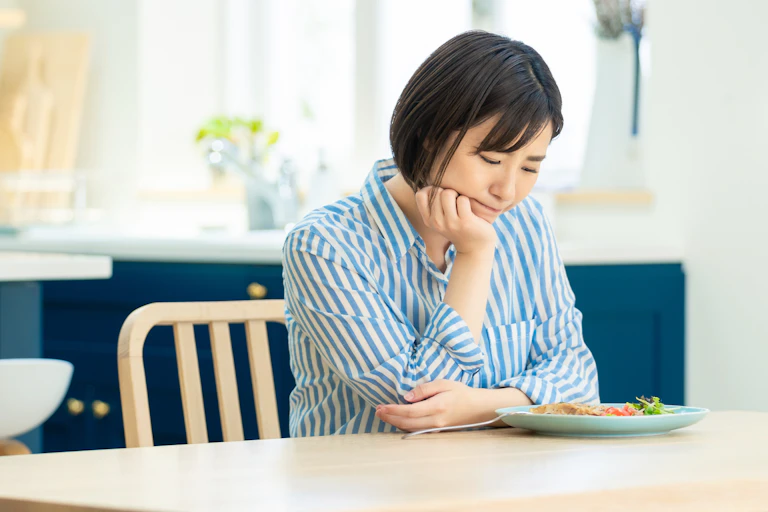 A woman looks sadly at the small plate of food in front of her.