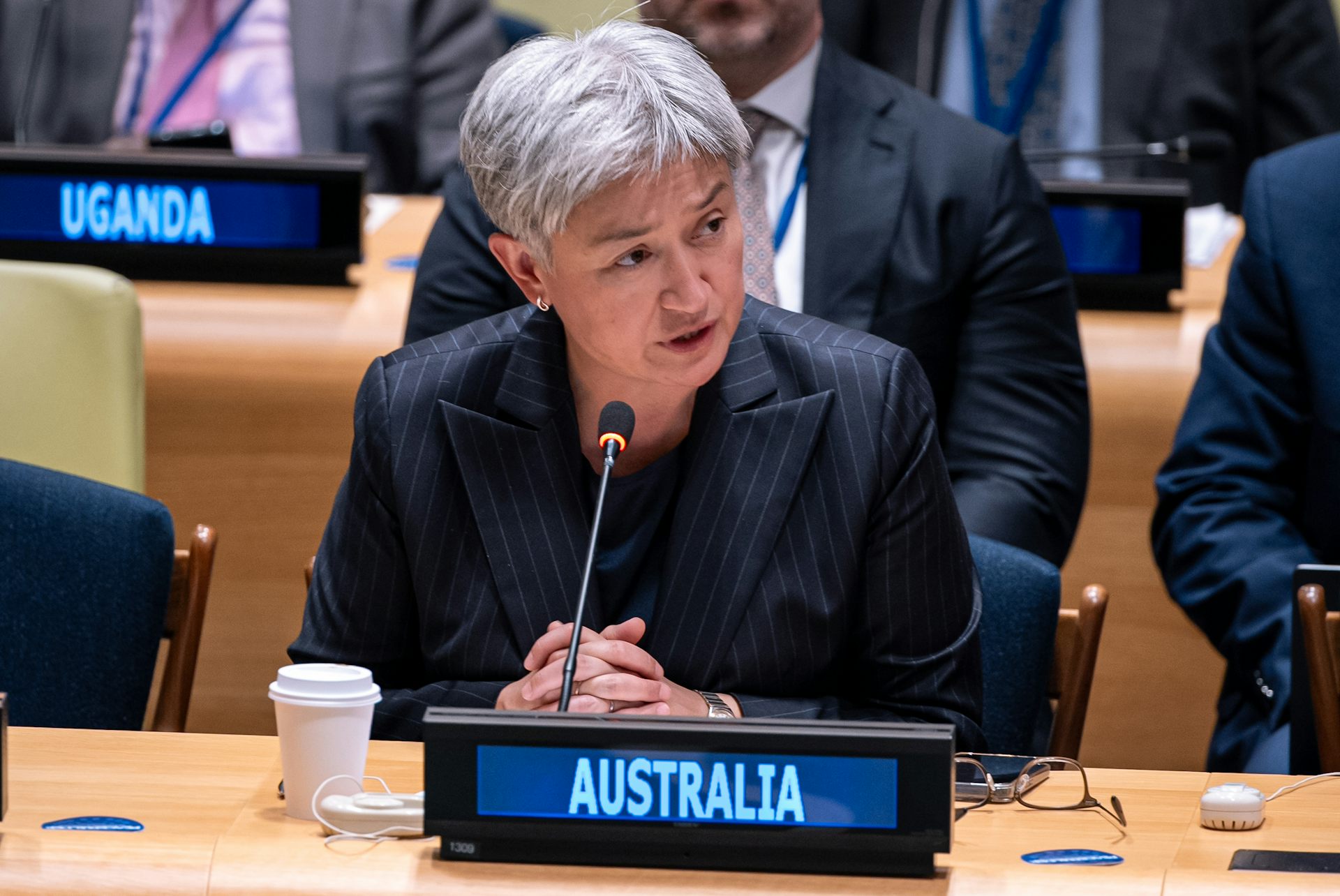 A woman with short grey hair sits at a desk behind an Australia sign.