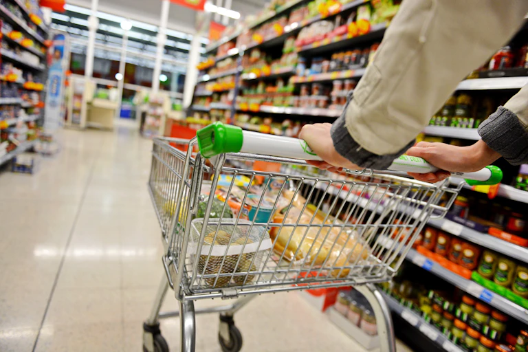 shopper pushing a shopping trolley down a supermarket aisle.
