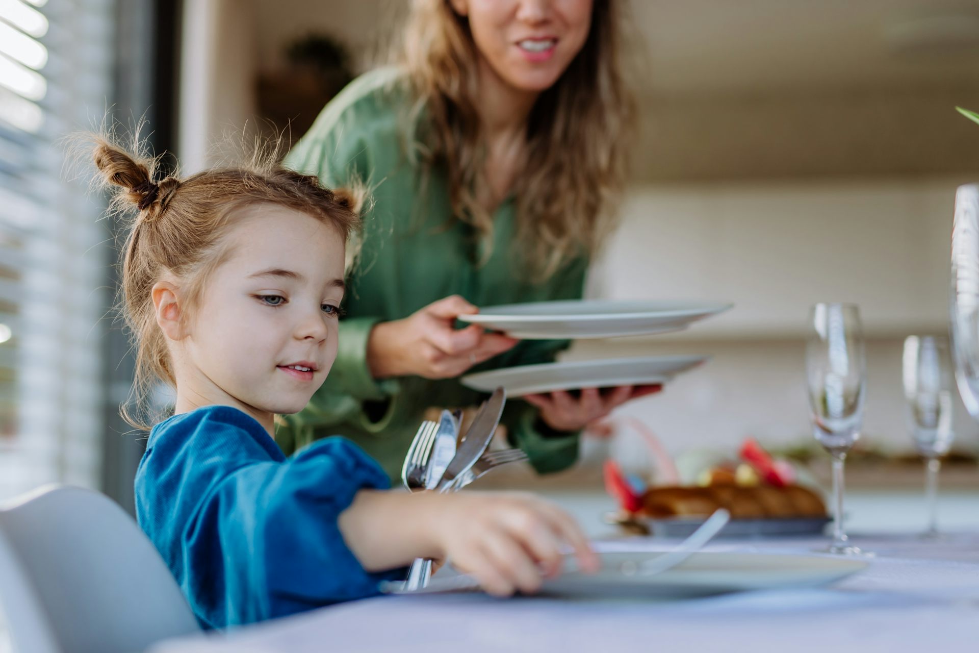 woman laying plates out in front of a young girl sitting at a table.