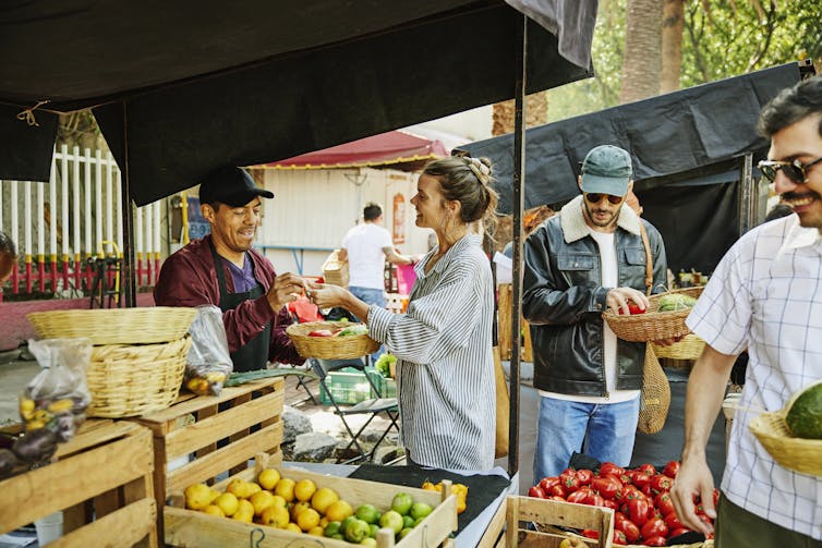 A fruit vendor talks with a customer by his display at a farmers market.
