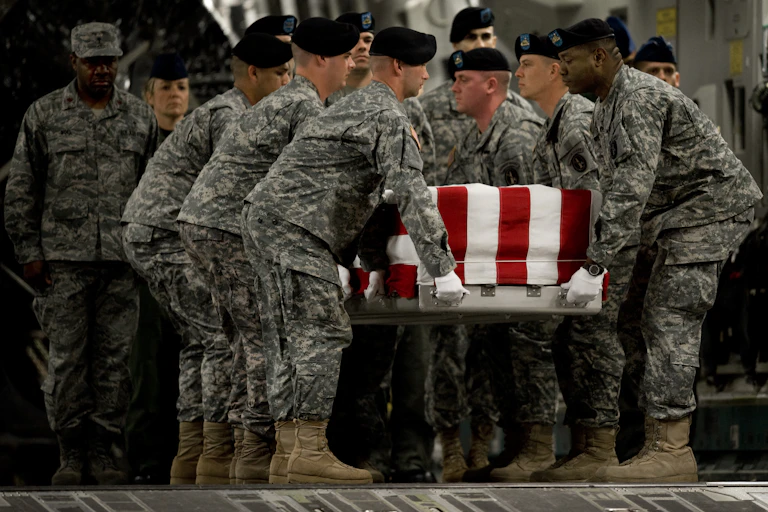 Soldiers in camouflage holding a flag-draped long box.