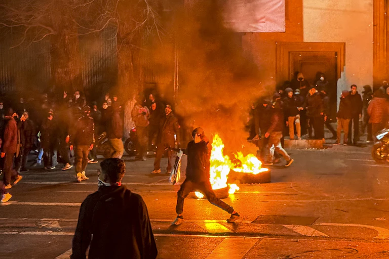 A protester in a mask stands in front of a fire.