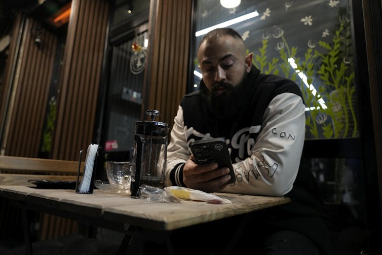 How social media is channeling well-liked discontent in Iran throughout ongoing duration of home unrest 2 A man looks at his phone at a cafe at night.
