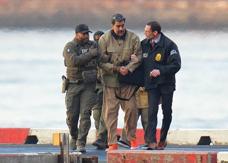 A man in handcuffs being moved along by uniformed law enforcement agents.