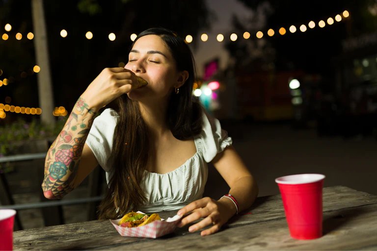 A young woman eats a taco at a bar's festive outdoor seating area.