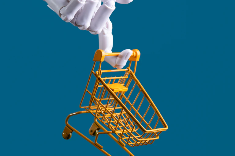 a robot hand dangles a toy shopping cart from its index finger