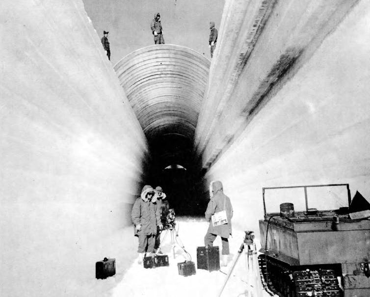 Military engineers building Camp Century wear parkas and stand in a tunnel wide enough to drive a truck through.