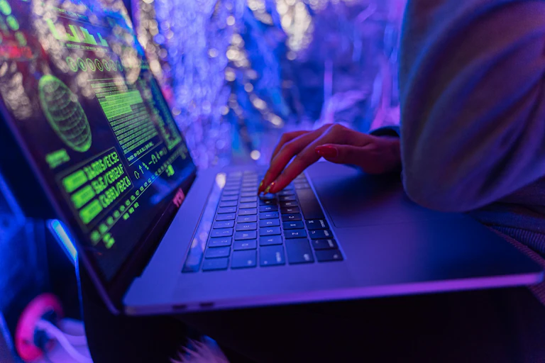 A person using a laptop computer under neon lights.