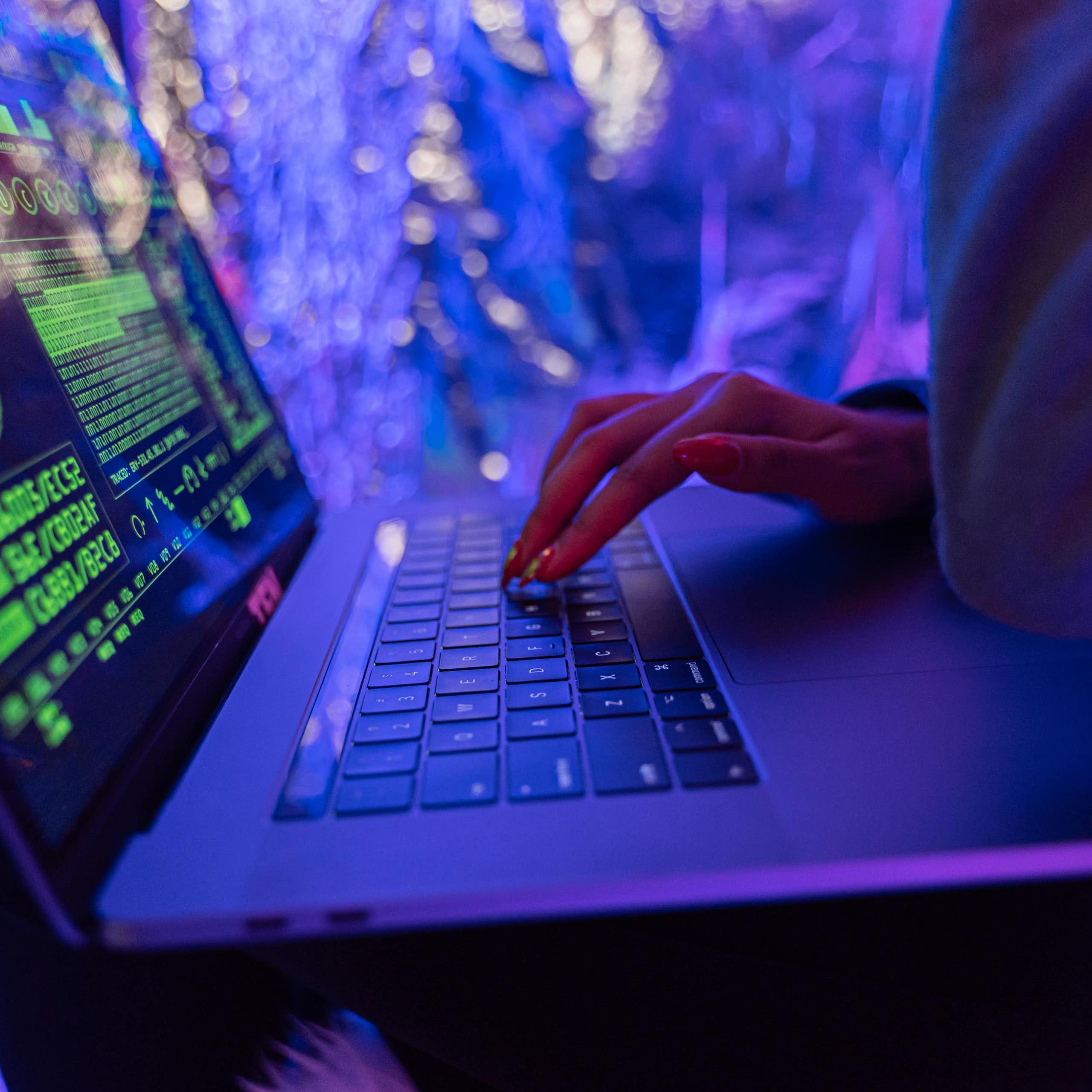 A person using a laptop computer under neon lights.