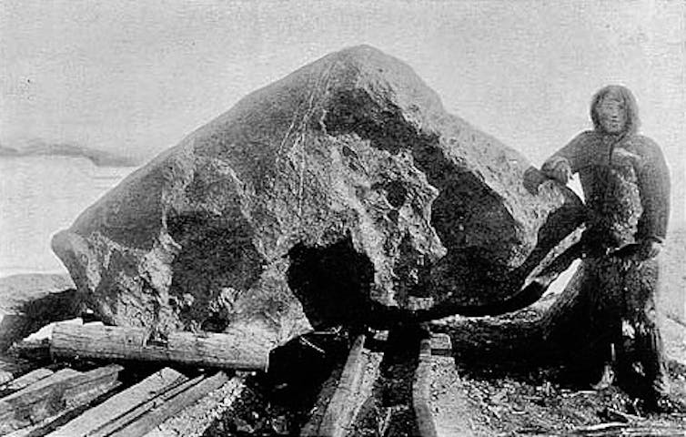 A man stands beside a very large rock almost as tall as he is