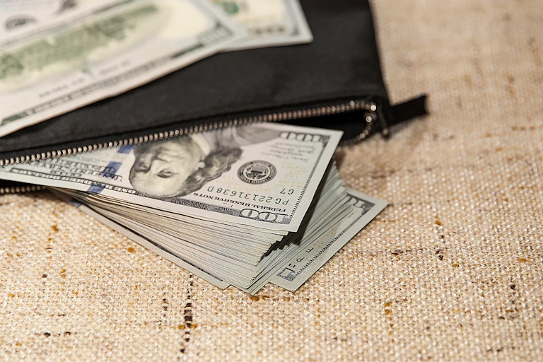 pile of 100 dollar bills poking out of a black wallet