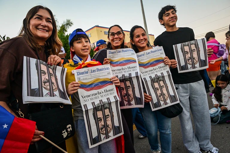 five people smiling and holding newspapers showing an illustration of Nicolas Maduro behind bars