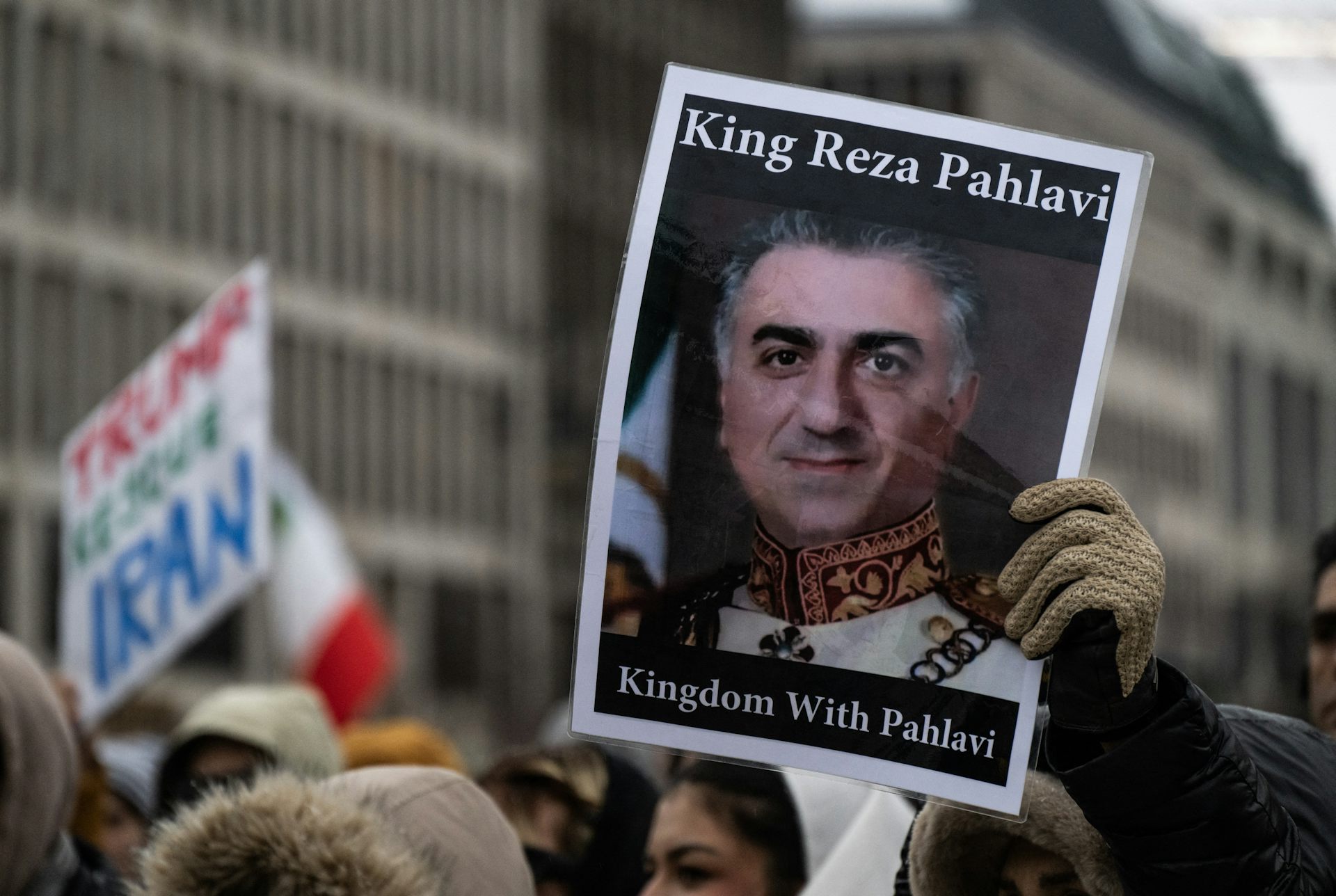 A protester holds aloft a photo of a man with 'King Reza Pahlavi' written above.