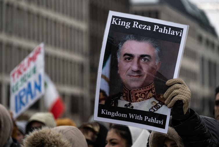 A protester holds aloft a photo of a man with 'King Reza Pahlavi' written above.