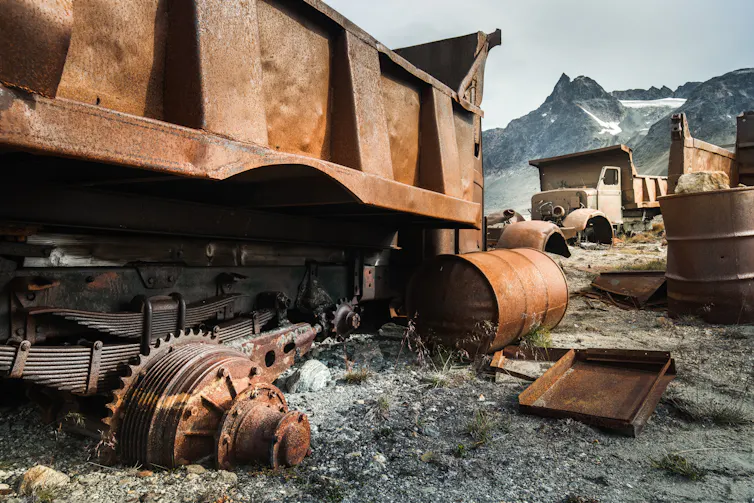 Large rusted construction trucks and some fuel drums.