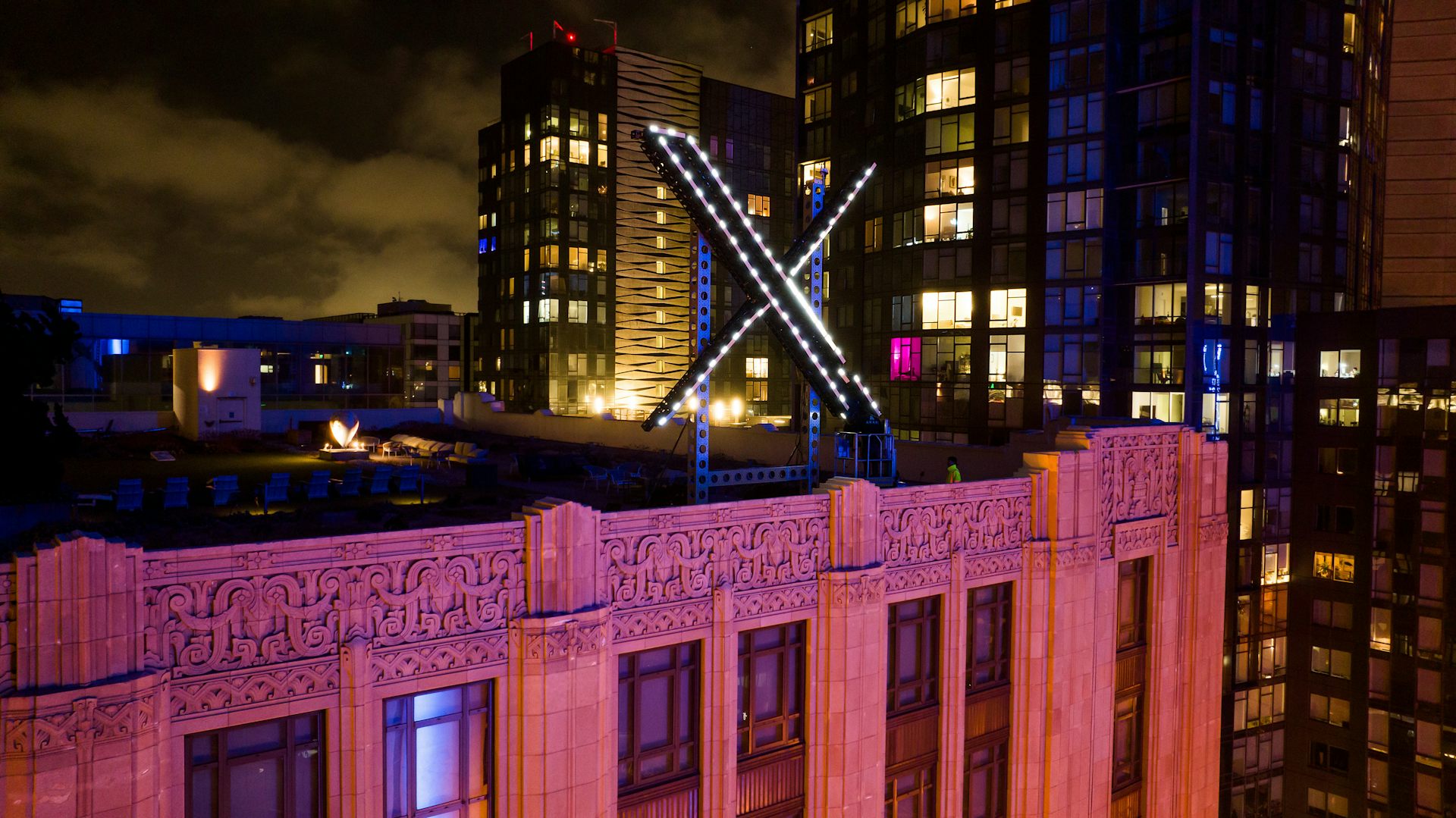 Workers install a large illuminated X on top of a building at night.
