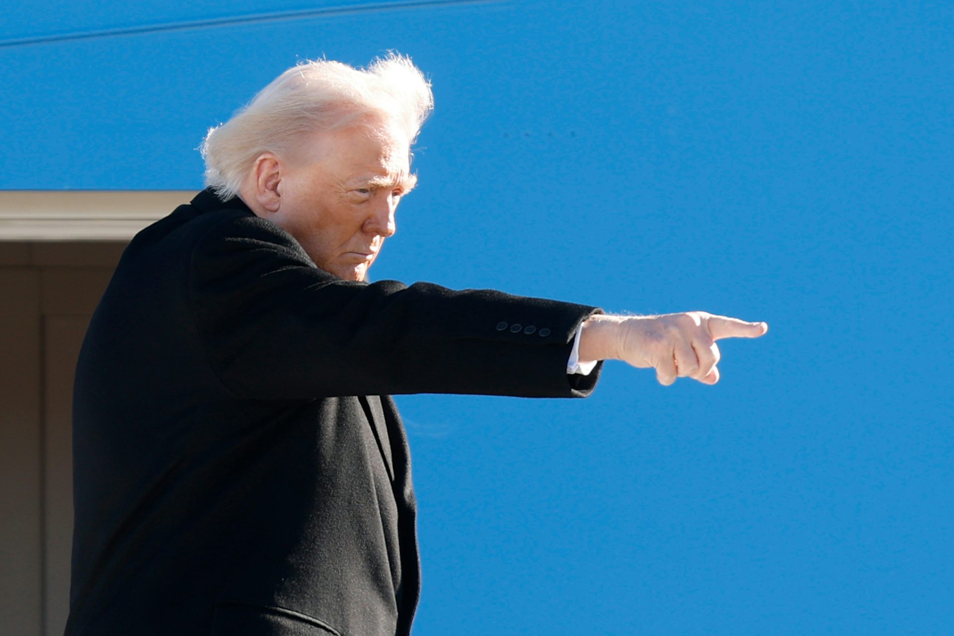 A man glowers and points as wind blows back his fluffy white hair.