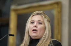 Una mujer rubia de cara redonda habla por un micrófono.