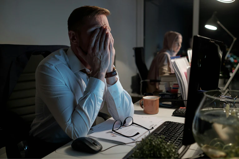 A man sitting at a desk covering his face with his hands