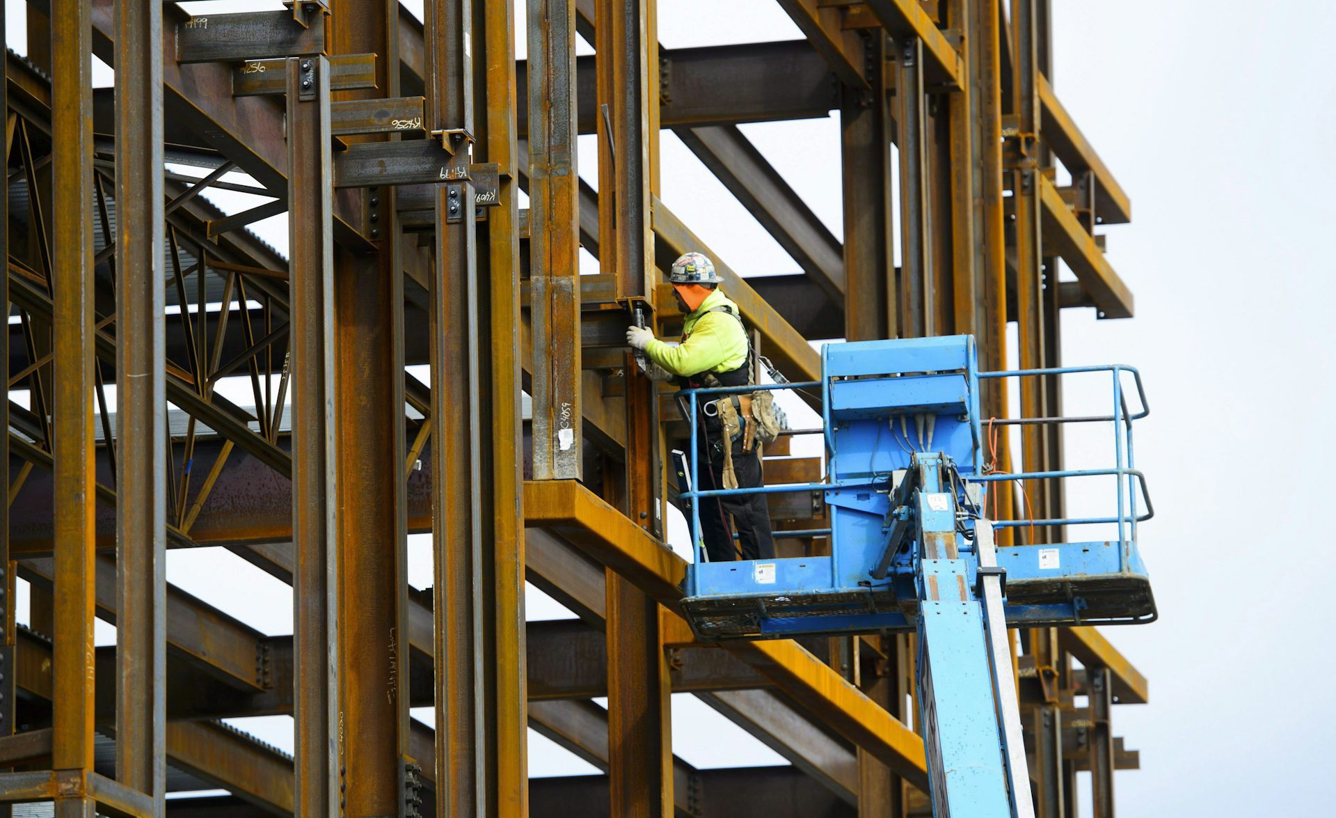 A construction worker stands on a platform working on a steel structure
