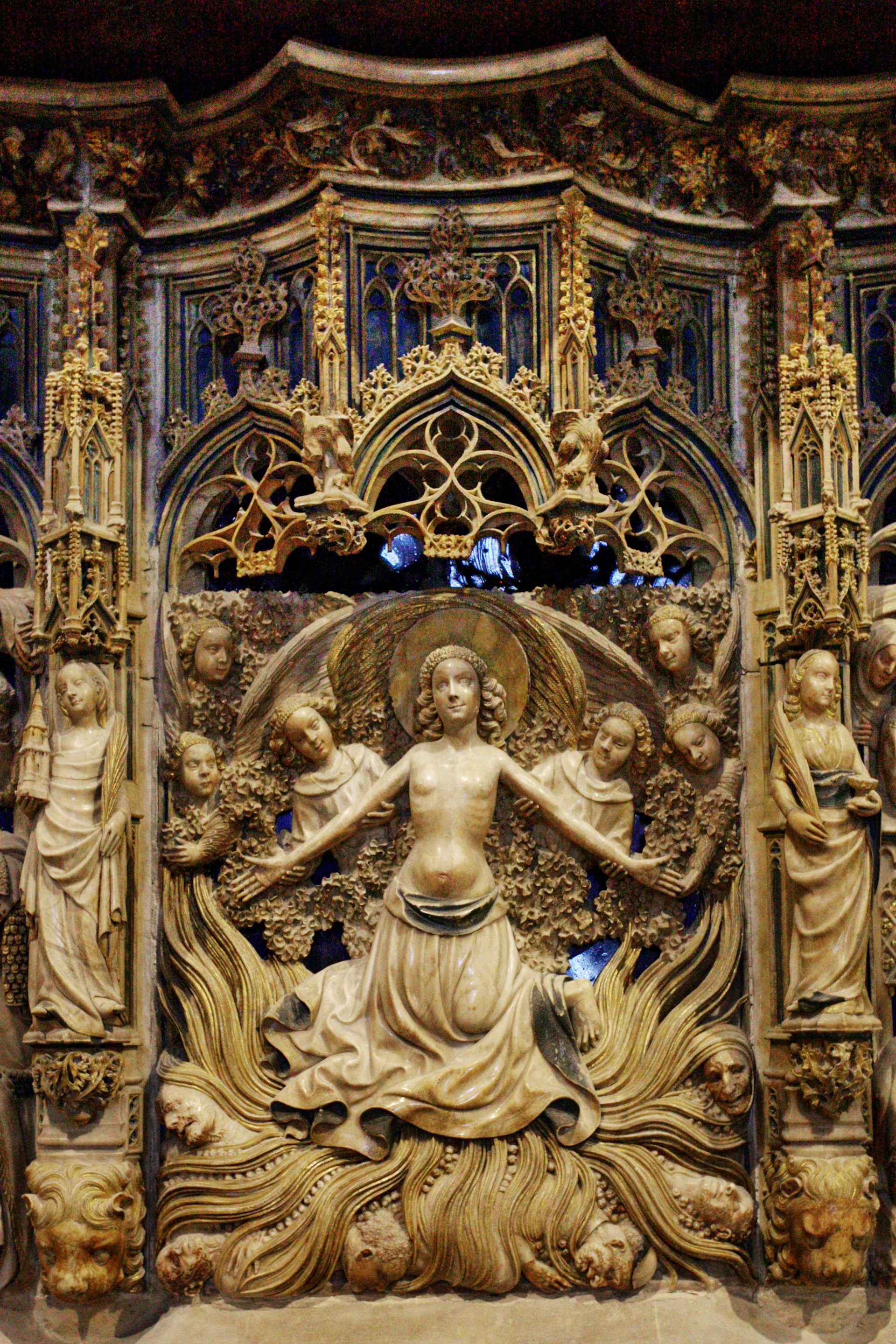 An ornate carving depicts a woman, stripped to the waist, who holds out her arms as she seems to stand atop flames.